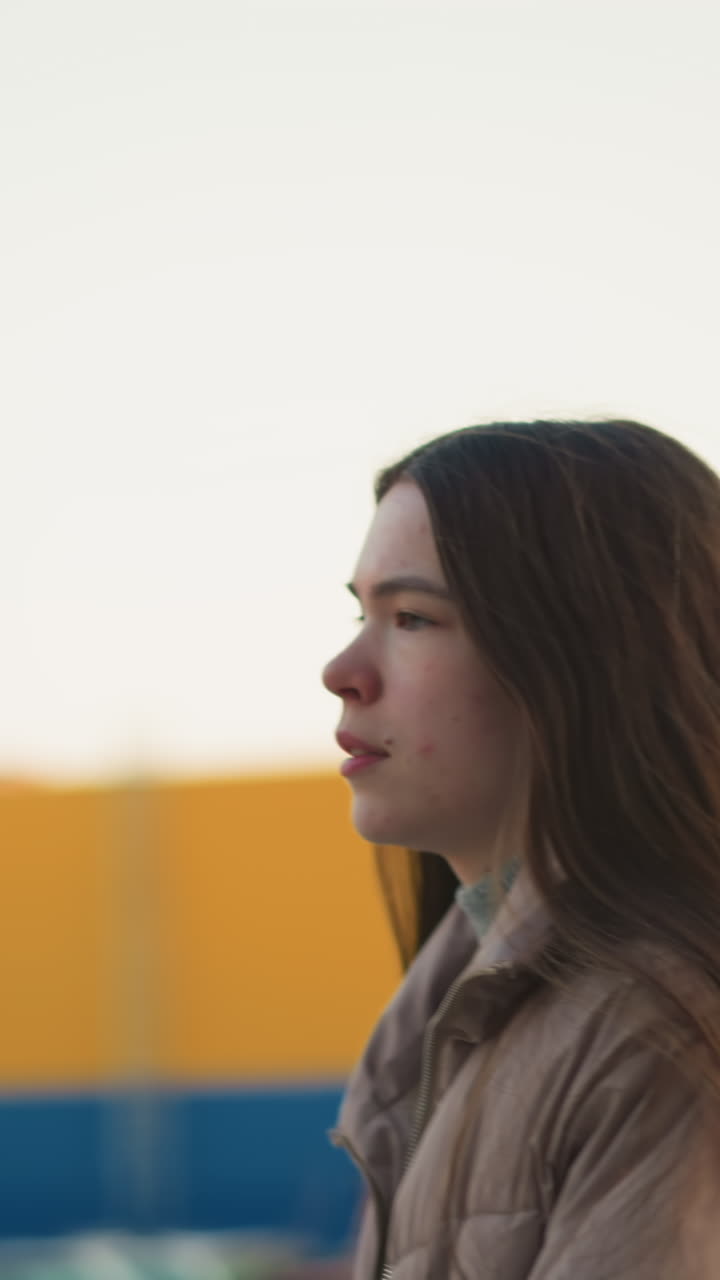una toma de primer plano de una joven con una chaqueta de melocotón, capturada durante una actividad al aire libre en un parque. la imagen destaca su parte superior del cuerpo y la expresión facial, en un fondo urbano borroso