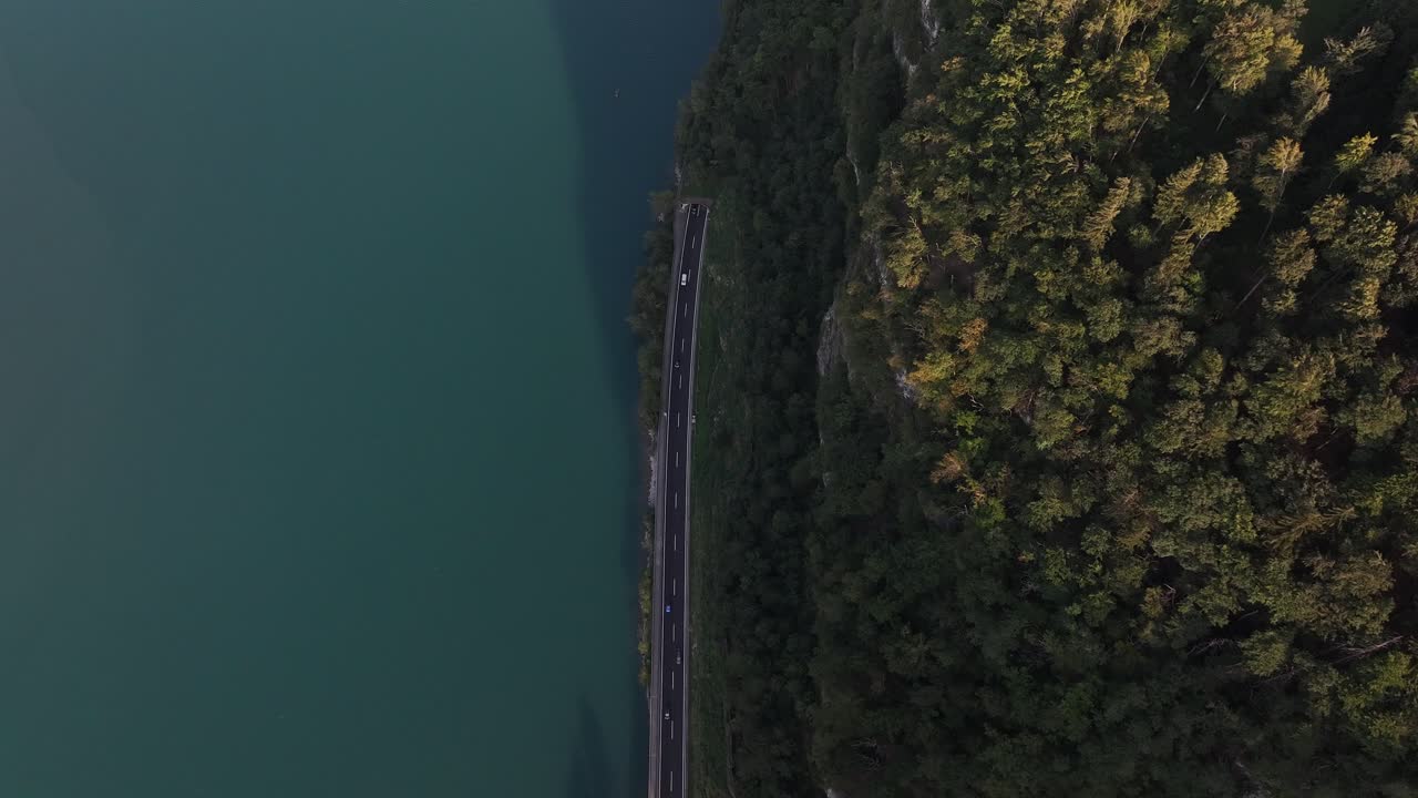 Auto che guidano lungo il lago Walensee e la montagna con fitta foresta a Filzbach, Glarus, Svizzera