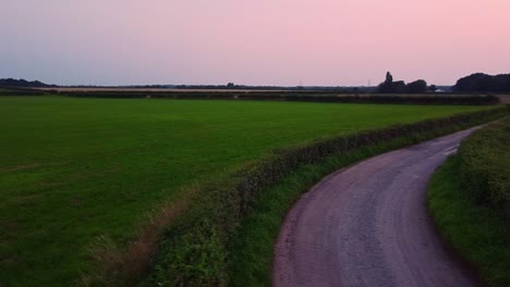 Drone-shot-of-country-lane-at-sunset-between-fields