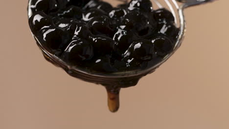 Close-up-on-Steel-Spoon-with-Sticky-Black-Tapioca-Pearls-Falling,-Soft-Background