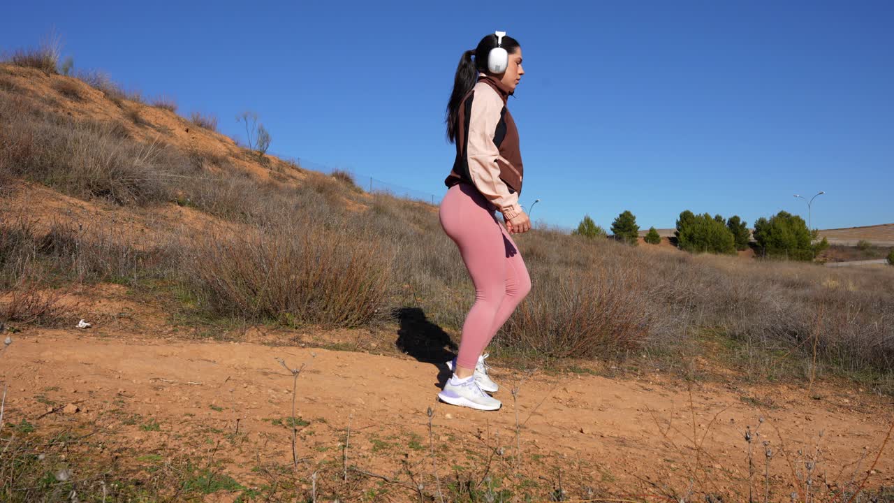 Woman with headphones stretches calves, then keeps running down on dusty path