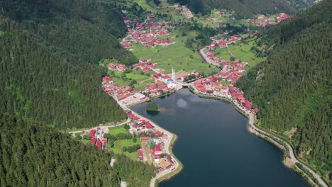 Vista-Aérea-De-Arriba-Hacia-Abajo-De-Un-Pueblo-De-Montaña-Lleno-De-Casas-Con-Techos-Rojos-Rodeados-De-Montañas-Y-Una-Mezquita-Cerca-De-Un-Gran-Lago-Ubicado-En-Uzungol-Trabzon-Turquía-En-Un-Día-Soleado-De-Verano