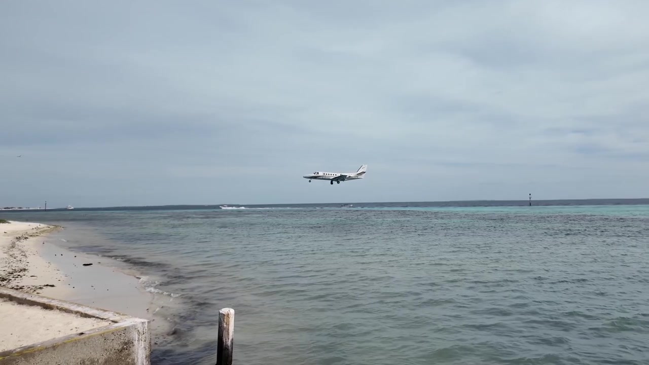 Lille fly nærmer sig landingsbane over turkis vand nær en tropisk ø-strandlufthavn