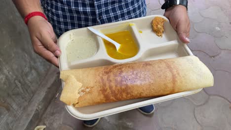 masala dosa, un plato popular del sur de la india preparado con arroz, lentejas, papas, methi y hojas de curry y servido con chutneys y sambar, se sostiene en la mano de un hombre