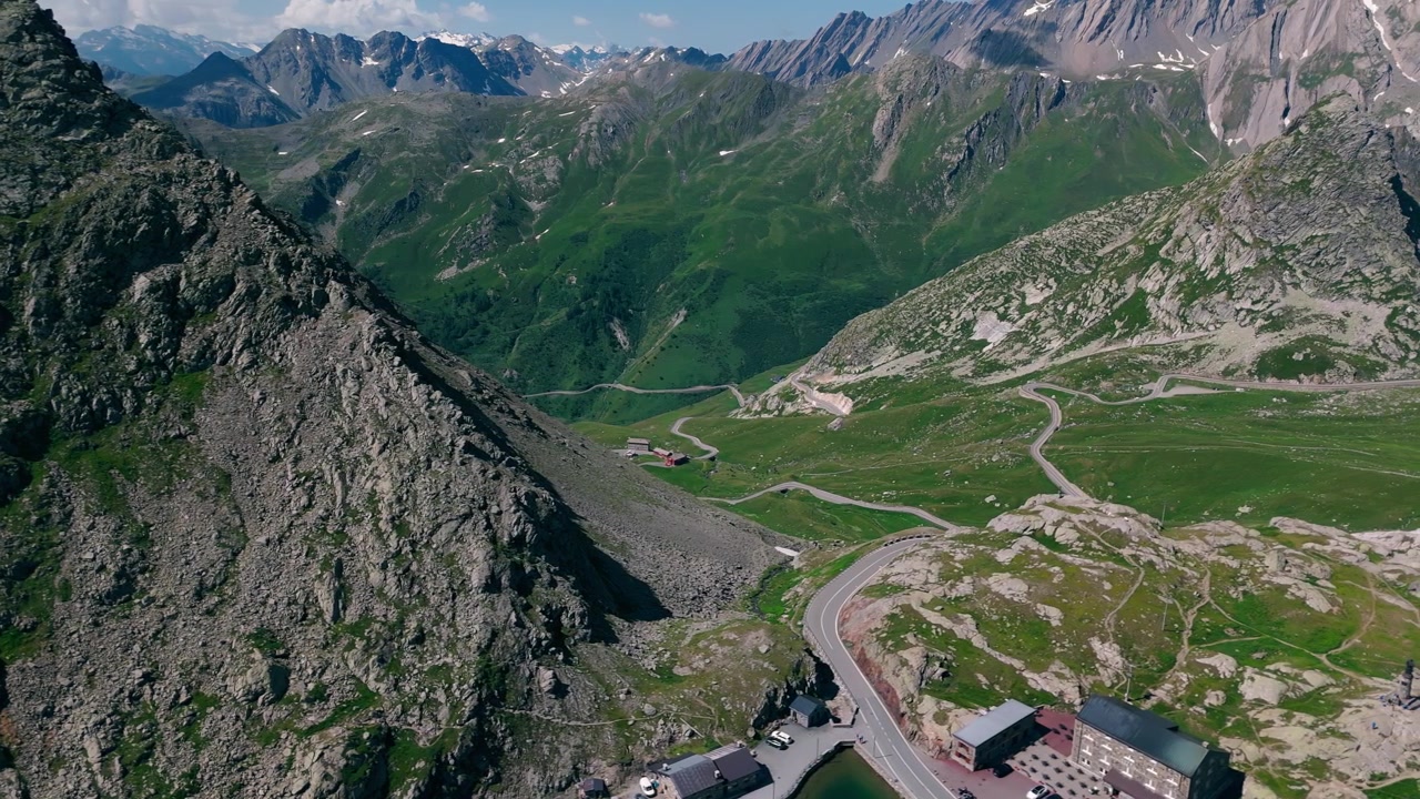 Büyük St Bernard Geçidi'nde kıvrımlı dağ yolu, göl ve engebeli zirvelerin havadan görünümü.