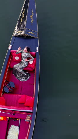 beautiful model in gondola. woman enjoys vacation while floating in a boat on water. luxury woman sailing in gondola. aerial view. vertical video
