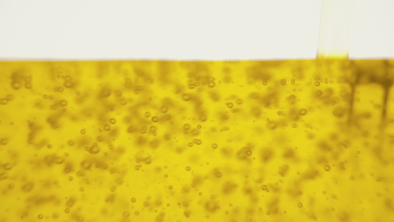 A line of yellow olive oil filling a jug over a white background, creating an intense appealing depiction, with air bubbles forming and rising