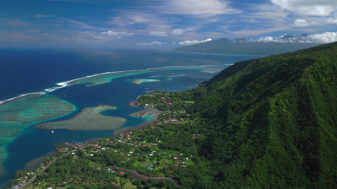 Koralrevsbølge ved Teahupo'o, nord-syd Tahiti-øerne, Fransk Polynesien. Luftfoto med drone af kysten en solrig morgen. Kanalen ved Papeete, Paris OL 2024 surf-venue med dommertårn og fremadgående panorering opad.