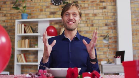 portrait of caucasian man making heart shape with hands while having a videocall at home