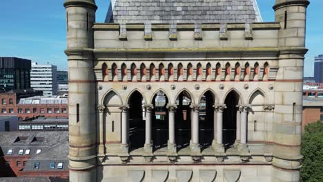 Vuelo-Aéreo-De-Drones-Pasando-Por-La-Torre-Del-Reloj-De-La-Corte-De-La-Corona-De-Manchester-Con-Una-Vista-Del-Horizonte-Del-Edificio-De-La-Torre-De-La-Ciudad-En-Los-Jardines-Piccadilly