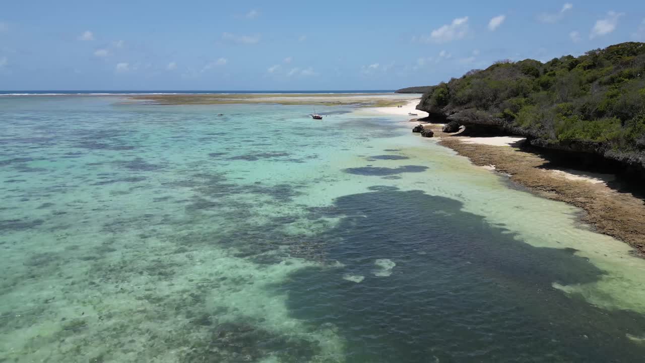 Shallow coral lagoon in Pungume Island Tanzania Africa southern Zanzibar with sailboat anchored, Aerial dolly in low shot