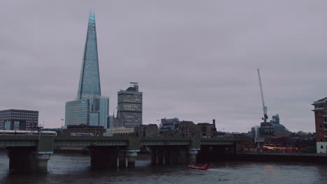 a wide shot of the shard and its bankside with a pub, a train leaving and boats passing