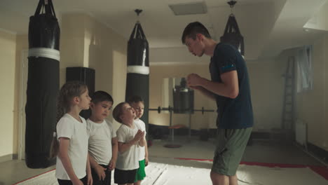 martial arts trainer teaches children in gym. little boy looks at instructor training with group in sports club slow motion. physical activity and self-defense