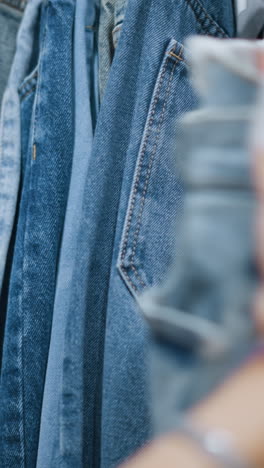 close-up of hand checking denim jeans in clothing store, exploring various shades and styles, showcasing texture and quality of denim, capturing focused shopping experience with casual fashion