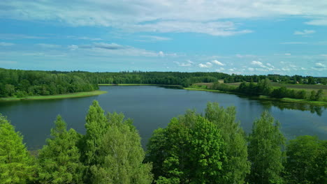 aerial drone forward moving shot over a lake surrounded by lush green forest on a bright sunny day