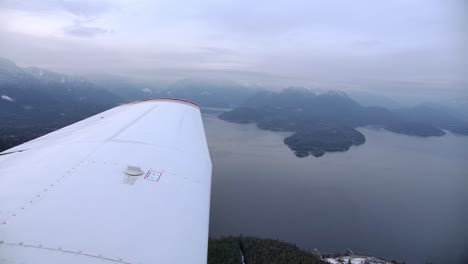 vista del ala de un avión ligero sobrevolando un lago de montaña - día nublado