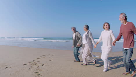 elderly men and women holding hands and running along beach