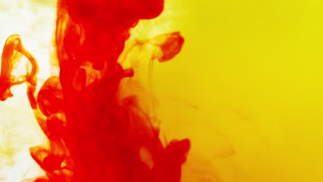 pintura o tinte rojo y amarillo caído en el agua contra un fondo blanco para crear un fondo de humo de colores giratorios