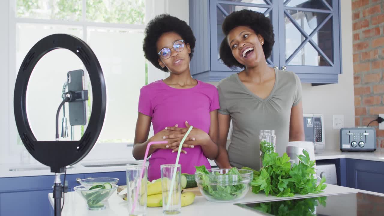 Lykkelig afroamerikansk mor og datter forbereder sund drik, optager video med smartphone
