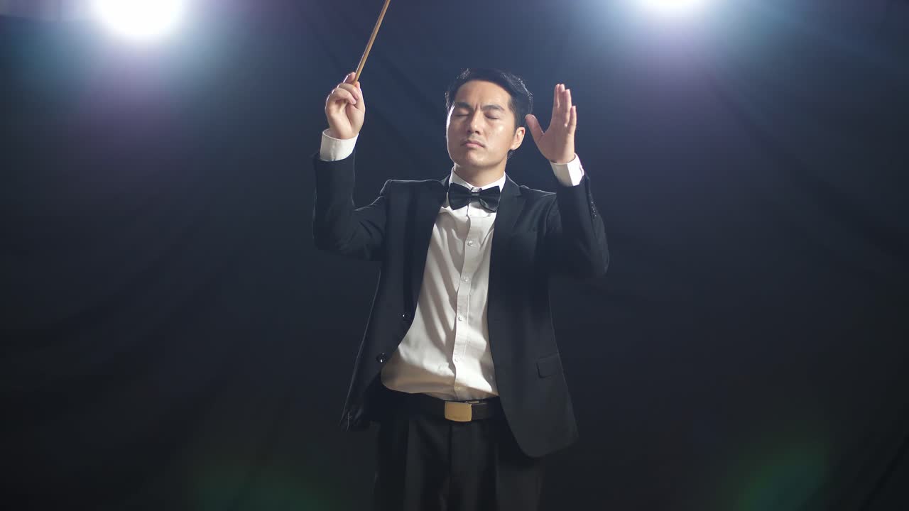 Asian Conductor Man Holding A Baton Closing His Eyes And Showing Gesture In The Black Studio