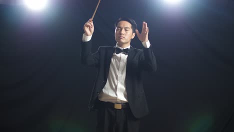 asian conductor man holding a baton closing his eyes and showing gesture in the black studio