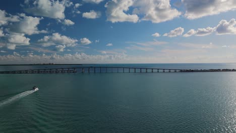 a powerboat sails towards the rickenbacker causeway bridge near miami, drone tracking shot sunny fair weather day