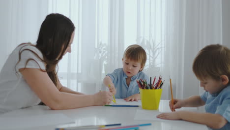 two children of boys draw with his mother sitting in the kitchen. happy family at home. brothers draw at the table. real people.