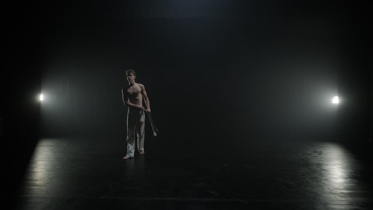 Capoeiristas realizando movimentos dinâmicos no palco. Artes marciais, dança e acrobacias em ação. Atletas sem camisa exibindo força, flexibilidade e técnica sob os holofotes
