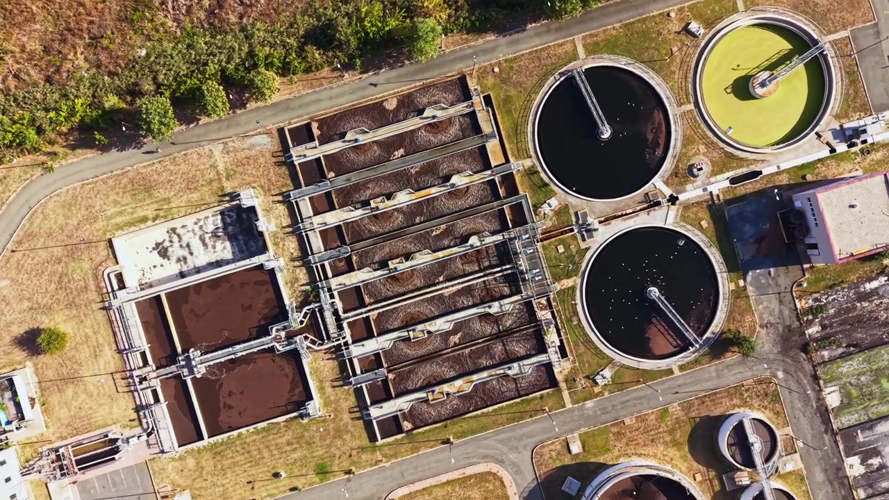 View of a wastewater treatment plant showing large rectangular tanks and circular basins during daylight