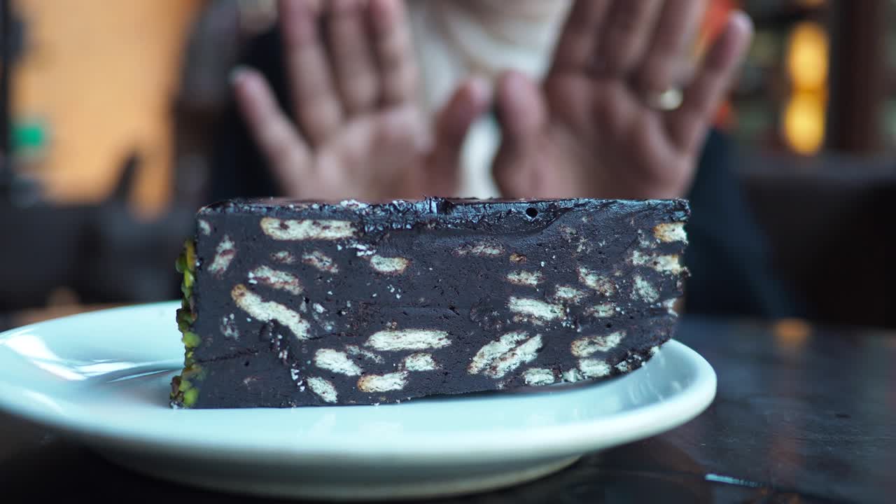 A close-up of a slice of mosaic cake on a white plate with a person in the blurred background