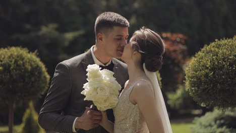 Newlyweds,-caucasian-groom-with-bride-walking,-embracing,-hugs-making-a-kiss-in-park,-wedding-couple