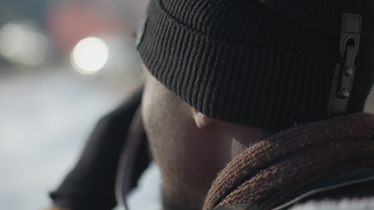 back view photographer wearing winter coat, beanie and scarf, gloved hands adjusting camera lens while walking snowy city street under winter sun, squinting eyes, blurred traffic