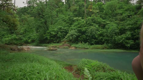 Fitte-Blonde-Frau,-Die-Am-Flussufer-Des-Ruhigen-Rio-Celeste-In-Costa-Rica-Spaziert