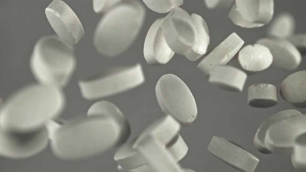 Pillole farmaceutiche bianche che cadono al rallentatore su uno sfondo grigio