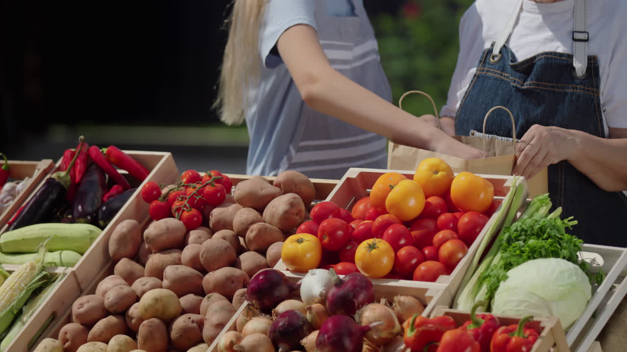 una mujer y su nieta venden verduras en el mercado - ponen tomates en una bolsa de papel. sólo las manos son visibles en el marco