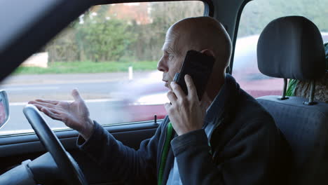 a mature man having car trouble is parked at the side of the road talking on his phone to a recovery company