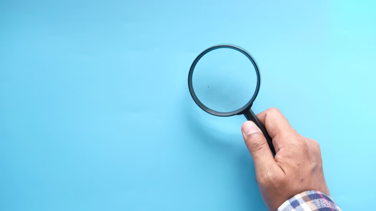 mano sosteniendo una lupa sobre un fondo azul claro