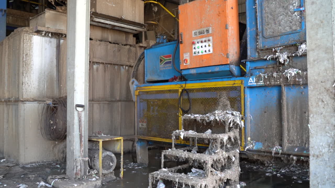 cinematic shot of recycling plant machinery with paper pulp on conveyor with a South African flag