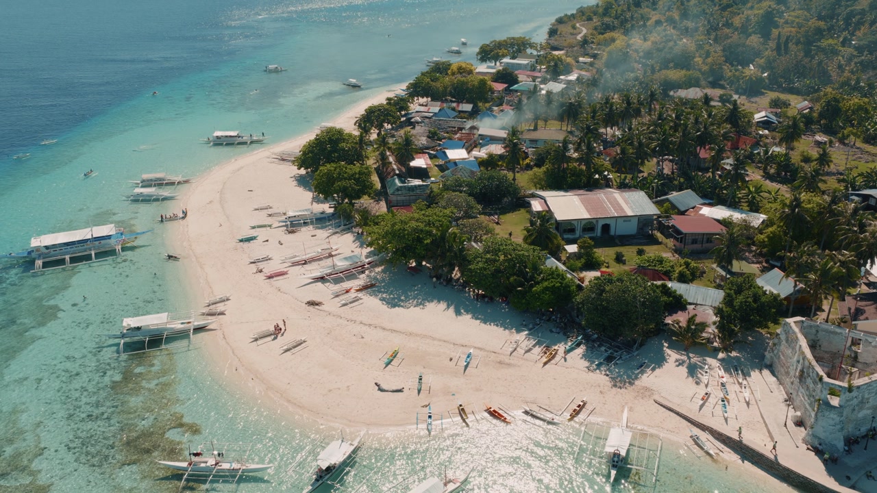 Aerial coastline of tropical village and beach with outrigger boats Pamilacan Island Bohol next to watchtower historic site