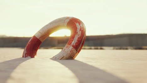 a red and white lifebuoy lies abandoned on a sandy beach at sunset