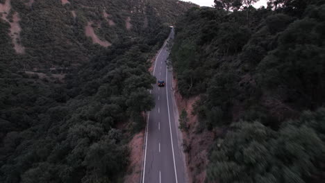 A-black-car-drives-along-a-remote-mountain-road-surrounded-by-forest