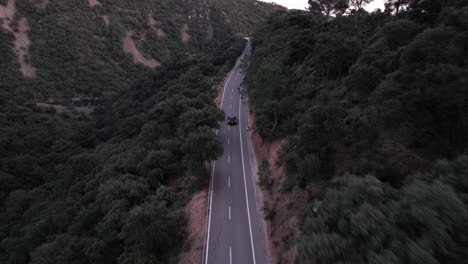 a black car drives along a remote mountain road surrounded by forest