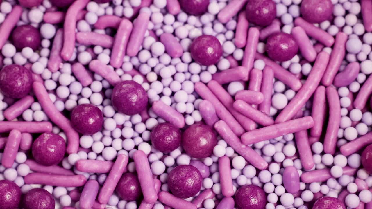 Close-up video of pink and purple sprinkles rotating, highlighting texture and color in a macro perspective