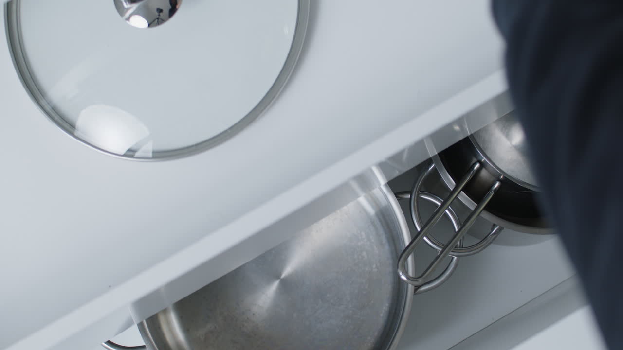 Opening a kitchen drawer with pots and a pan, putting away a small pot and opening another drawer within the drawer to put away the lid