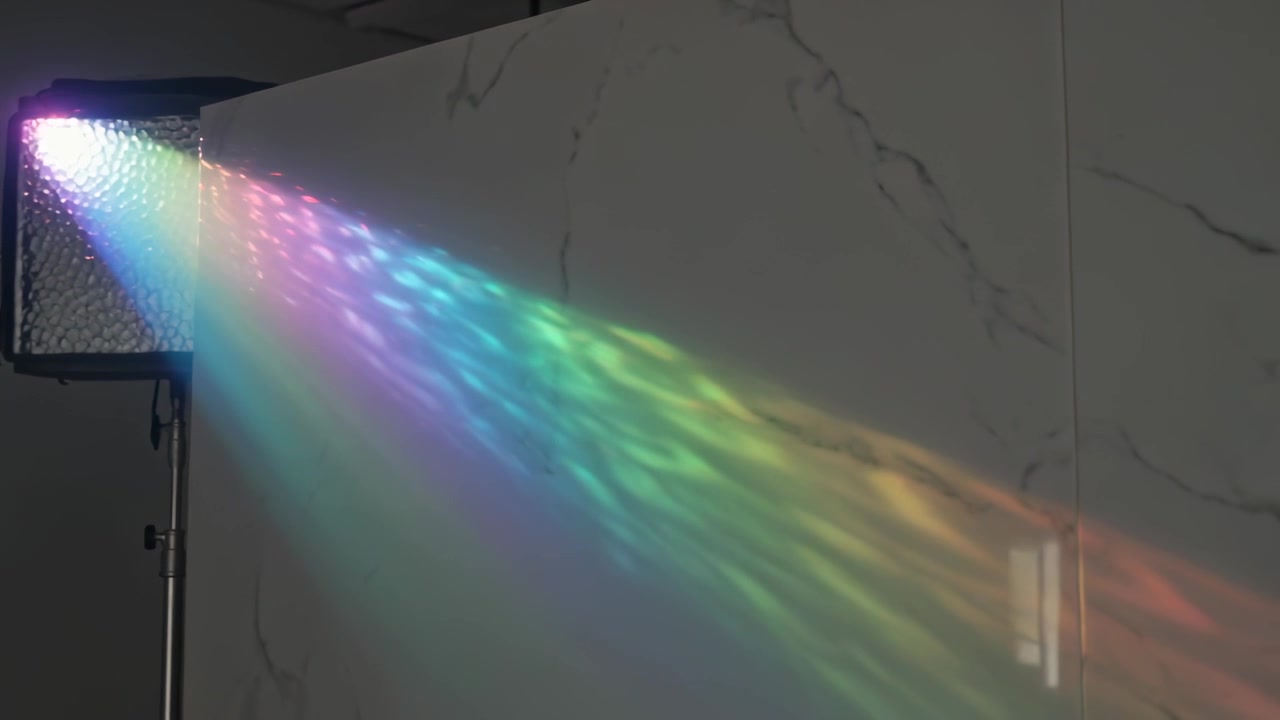 Accensione di un pannello LED che proietta un raggio arcobaleno su una parete di marmo, estendendosi a destra con una striscia sovrapposta.