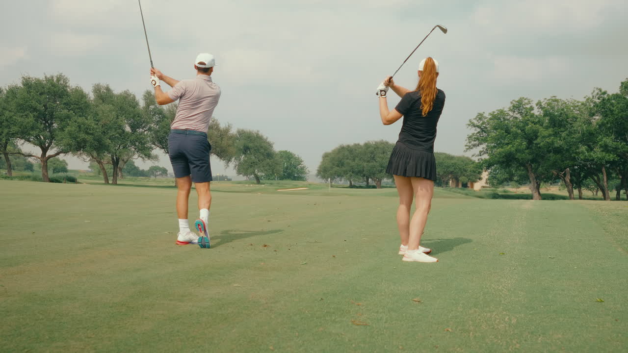 Golf couple hits fairway shots simultaneously in slow motion, showcasing synchronized swings and playfulness on a scenic course. A dynamic, energetic moment capturing difference in swings