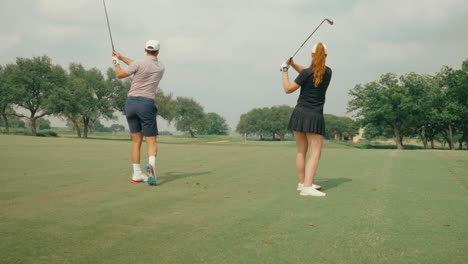 golf couple hits fairway shots simultaneously in slow motion, showcasing synchronized swings and playfulness on a scenic course. a dynamic, energetic moment capturing difference in swings