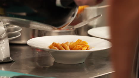 plating freshly cooked penne pasta at the restaurant kitchen for serving - close up, slow motion