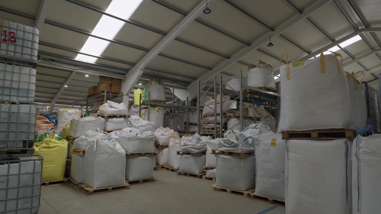 Wide recycling warehouse interior packed with rows of white bulk bags on wooden pallets under steel roof