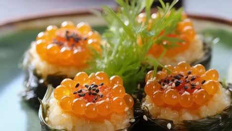 close up of salmon roe nigiri sushi. featuring glistening orange roe atop seasoned rice. wrapped in seaweed. garnished with black sesame seeds. and a sprig of fresh greens. presented on a green plate
